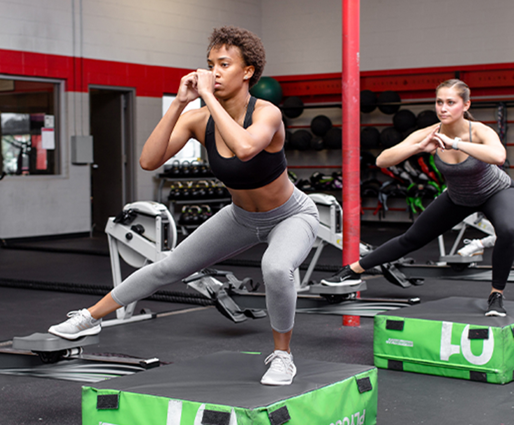 photo of two women in workout clothing squatting in gym