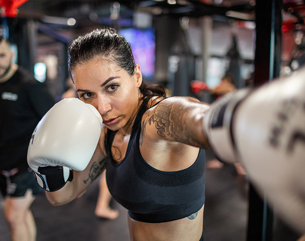 photo of woman in black workout clothing punching with white boxing gloves
