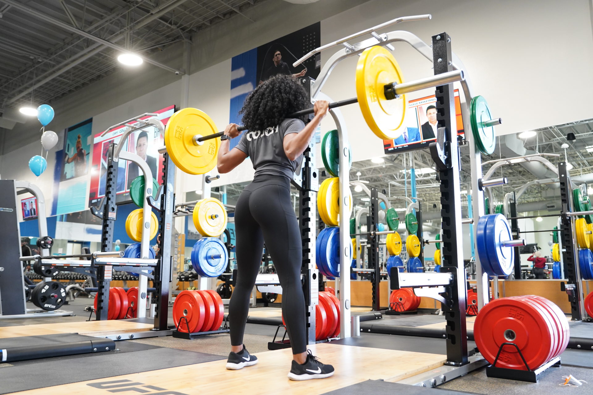 photo of woman in gray and black workout clothing using yellow barbell