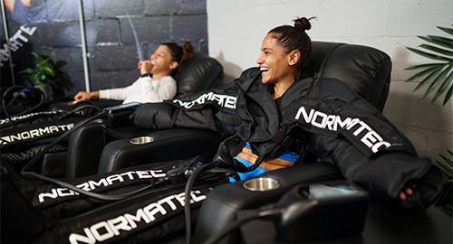 photo of two women in workout clothing using massage chairs