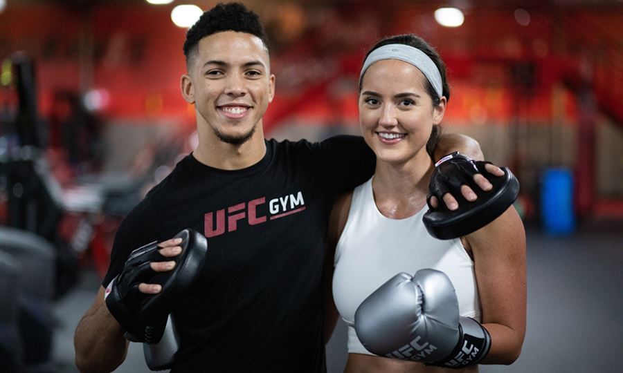 Image of smiling woman and man in UFC GYM shirts and silver boxing gloves
