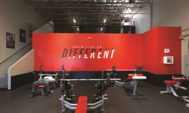 Image of UFC GYM franchise interior with a red wall that says “train, live, be different.”