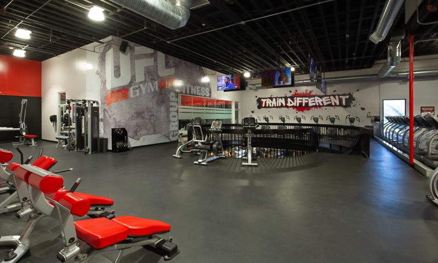 The interior of a UFC GYM location with red equipment, gray floor and “train different” on the wall