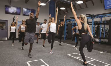 A group of UFC GYM members stretching with one arm and one leg raised.